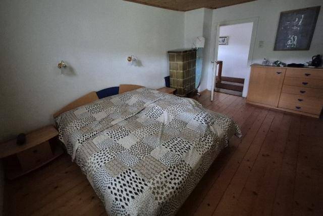 Schlafzimmer mit Doppelbett, Holzboden und traditionellem Kachelofen für gemütliche Wärme.
