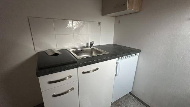 Kompakte Küchenzeile mit Spülbecken, dunkler Arbeitsplatte und integriertem Kühlschrank, ideal für kleine Wohnungen.