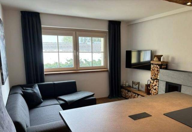 Gemütliches Wohnzimmer mit dunklem Ecksofa, Fernseher und integriertem Holzlager für den Kamin.