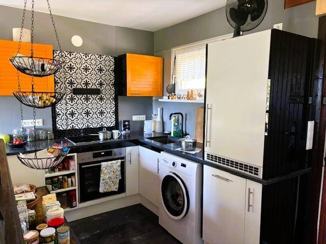 Moderne Küche mit orangefarbenen Akzenten, Waschmaschine und gemusterter Rückwand.
