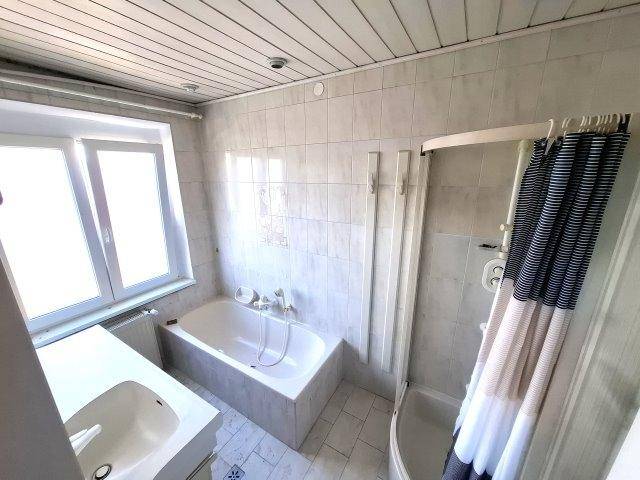 Gefliestes Badezimmer mit Badewanne, Dusche, Einzelwaschbecken und einem Fenster.