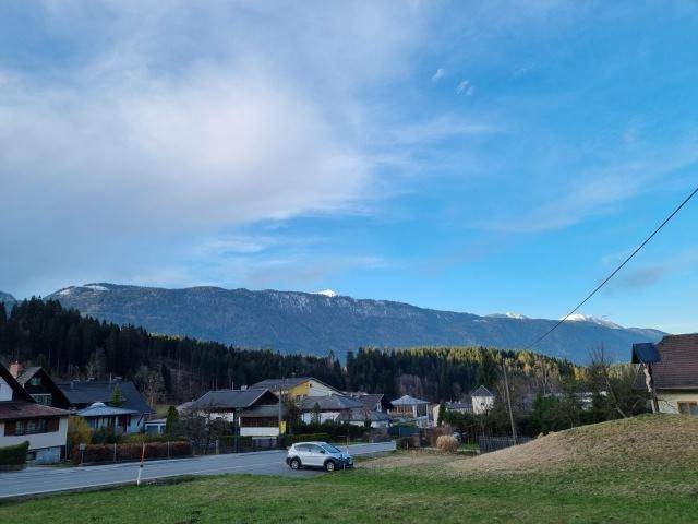 Weitläufiger Blick über eine ländliche Siedlung mit schneebedeckten Bergen unter blauem Himmel.