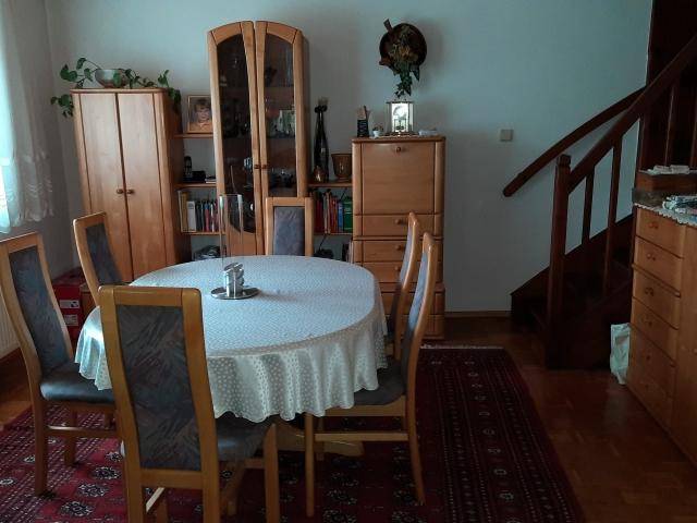 Gemütlicher Essbereich mit Holztisch, Stühlen und Teppichboden neben einer Holztreppe.