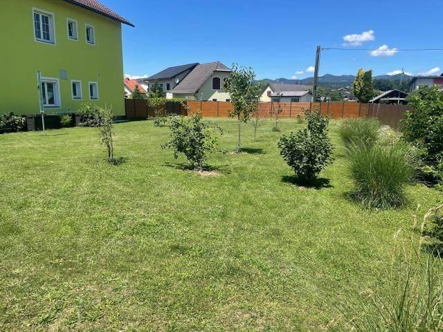 Großer, gepflegter Garten mit Rasenfläche und jungen Bäumen, umzäunt von einem Holzzaun.