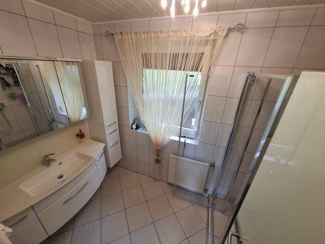Modernes Badezimmer mit weißen Fliesen, Waschtisch, Duschkabine und Fenster für Tageslicht.