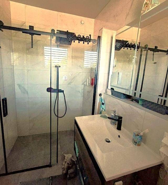 Modernes Badezimmer mit begehbarer Dusche, eleganten Fliesen und einem einzelnen Waschbecken.