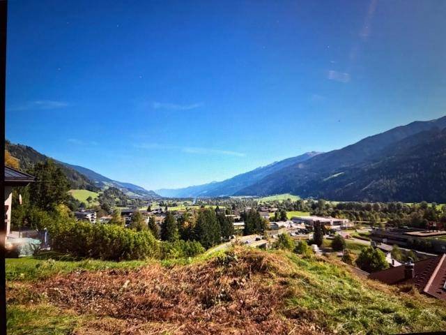 Weitläufiger Ausblick auf ein sonniges Tal mit einer Ortschaft und imposanten Bergketten.