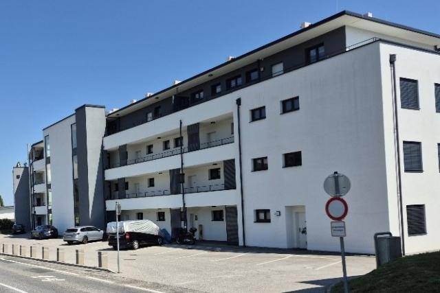 Modernes Mehrfamilienhaus mit weißer Fassade, Balkonen und Außenparkplätzen.