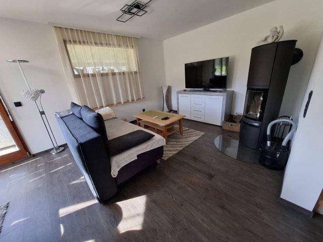 Gemütliches Wohnzimmer mit modernem Holzofen, Sofa und Fernseher.