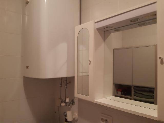 Badezimmerdetail mit Warmwasserboiler, Spiegelschrank und weißen Fliesen, funktional und hell.