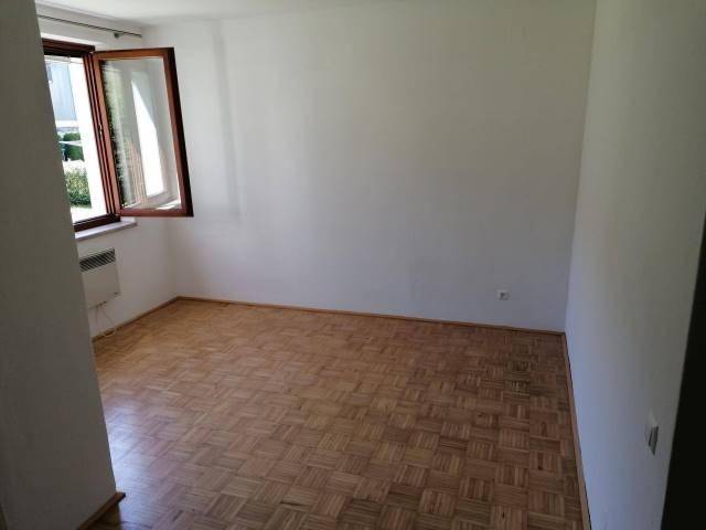 Heller, leerer Raum mit Parkettboden und einem geöffneten Fenster, das Tageslicht hereinlässt.
