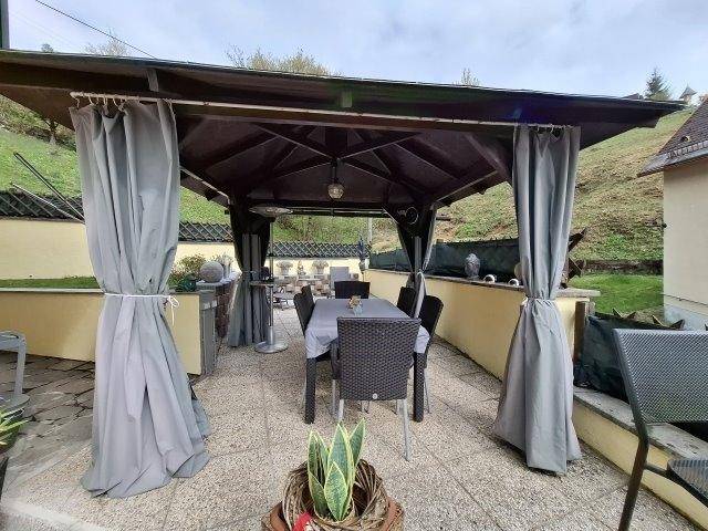 Gemütliche überdachte Terrasse mit Esstisch, Stühlen und Vorhängen für entspannte Stunden im Freien.