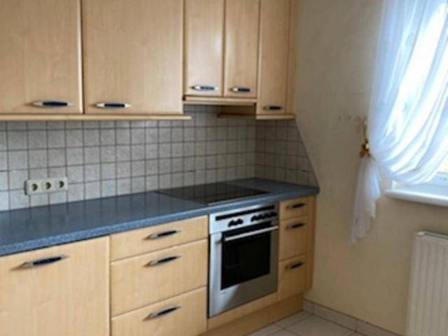 Funktionale Küche mit hellen Holzschränken, grauer Arbeitsplatte und integriertem Backofen.