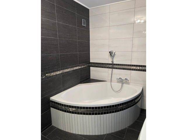 Modernes Badezimmer mit Eckbadewanne und schwarz-weißen Fliesen.