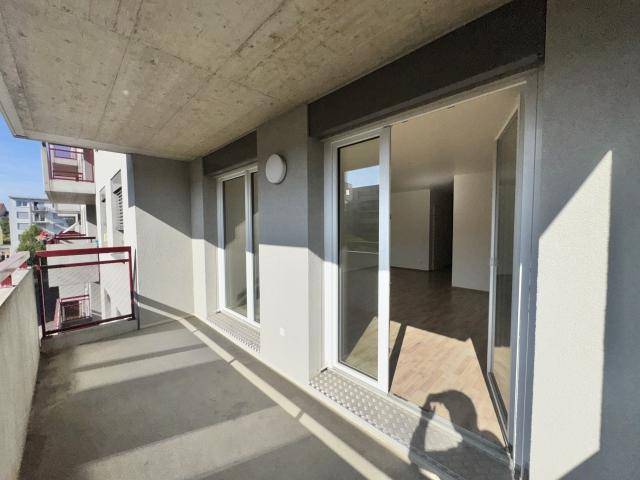 Geräumiger Balkon mit rotem Geländer und Schiebetüren, die den Blick in den hellen Innenraum freigeben.
