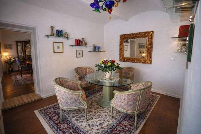 Eleganter Essbereich mit rundem Glastisch, verzierten Stühlen und einem großen Wandspiegel.