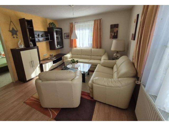 Helles Wohnzimmer mit beigen Ledersofas, Holzboden und dekorativen Elementen.