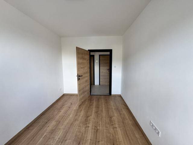 Leeres Zimmer mit Laminatboden und weiß gestrichenen Wänden, offener Zugang zu einem angrenzenden Flur.