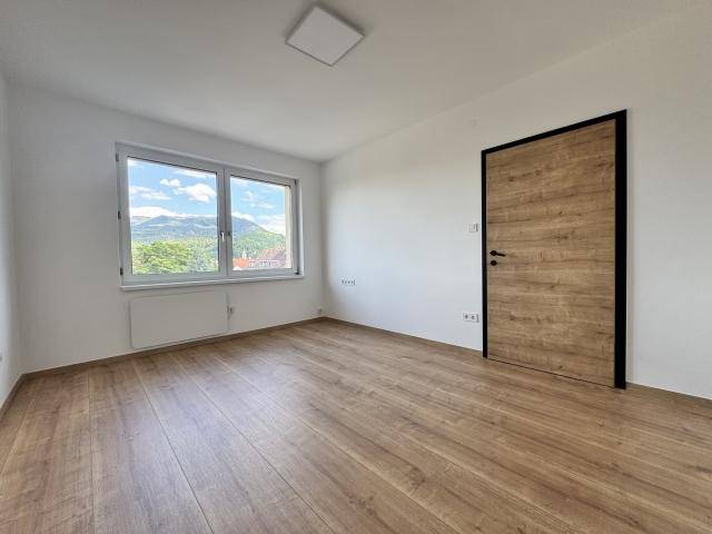 Helles Zimmer mit Laminatboden, weißen Wänden und einem Fenster mit weitem Bergblick.