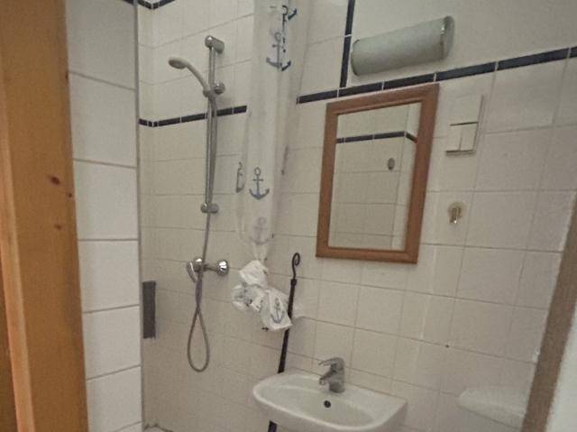 Kleines Badezimmer mit weißen Fliesen, Dusche und einem einzelnen Waschbecken.