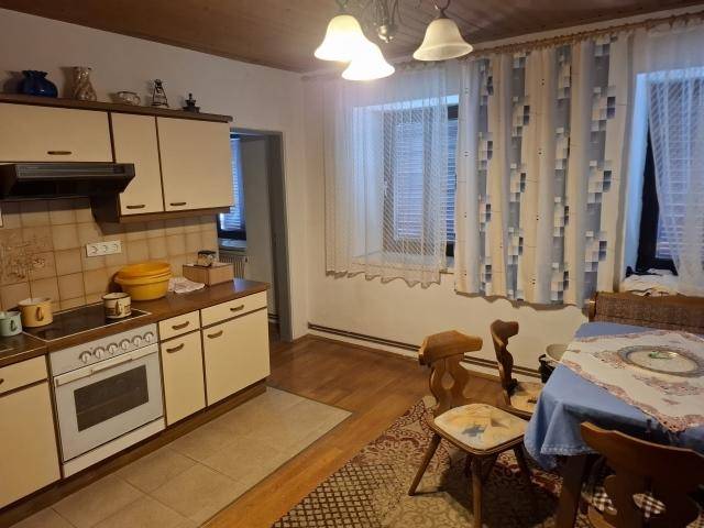 Traditionelle Küche mit Einbaugeräten, Essbereich und Holzdecke, hell durch Fenster.