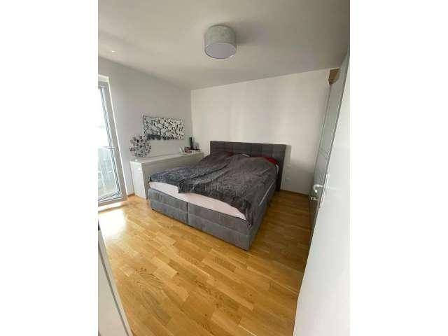 Helles Schlafzimmer mit Doppelbett, Holzboden und Zugang zu einem französischen Balkon.