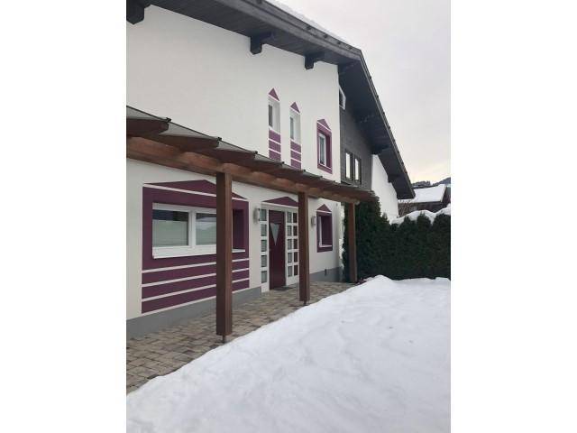 Seitenansicht des Hauses im Winter mit Schnee und überdachtem Eingangsbereich.