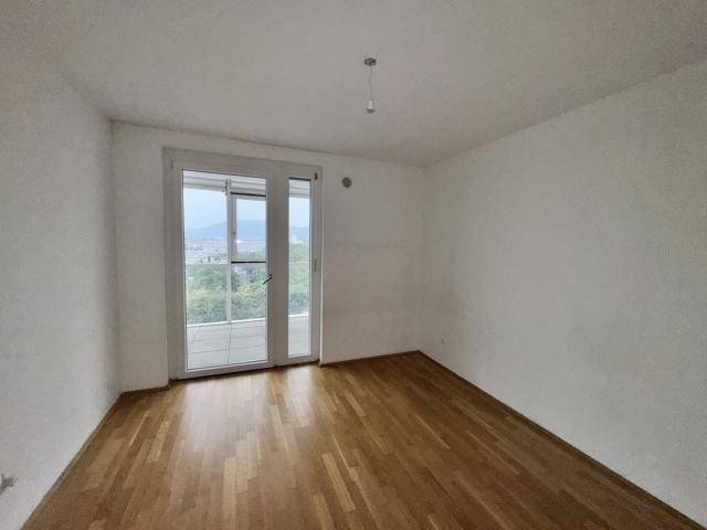 Heller, leerer Raum mit Parkettboden und Zugang zu einem potenziellen Balkon oder einer Terrasse.