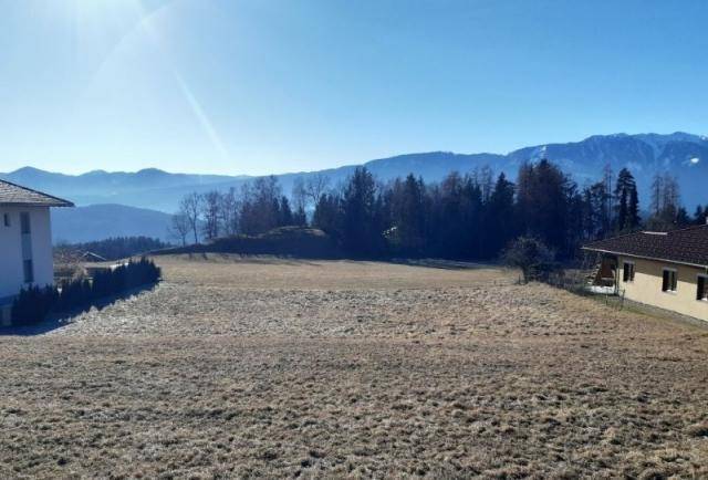 Weitläufiges trockenes Feld mit Blick auf eine weite Berglandschaft unter klarem blauem Himmel.