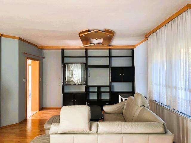 Gemütliches Wohnzimmer mit beigem Sofa, großer schwarzer Schrankwand und Holzfußboden.