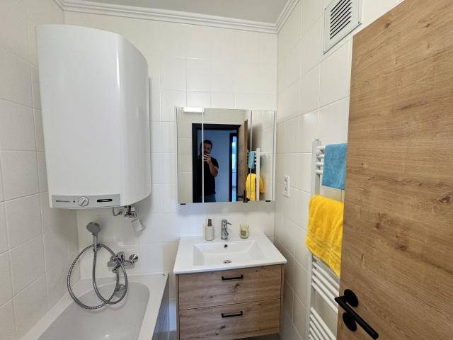 Modernes Badezimmer mit weißen Fliesen, Badewanne mit Duschfunktion, Waschtisch und beheiztem Handtuchhalter.