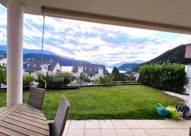 Überdachte Terrasse mit Gartenblick und weitem Ausblick auf den See und die umliegenden Berge.