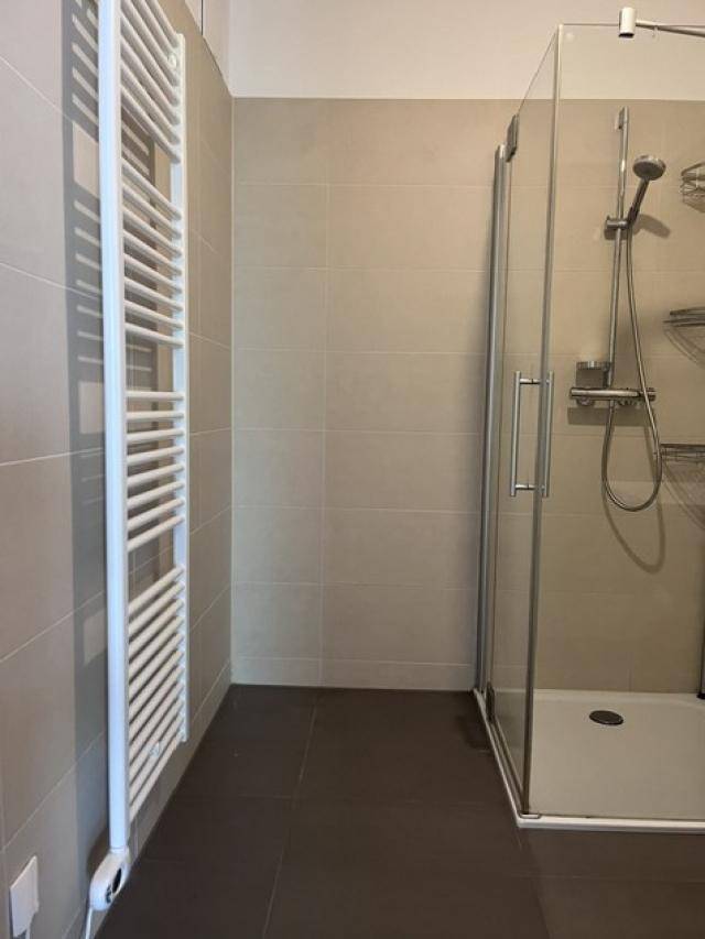 Modernes Badezimmer mit ebenerdiger Dusche, hellen Fliesen und beheiztem Handtuchhalter.