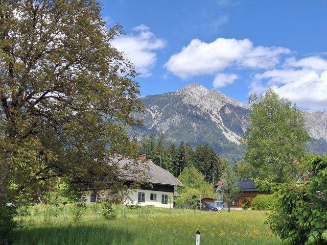 Idyllisches Haus in grüner Landschaft mit majestätischem Bergblick unter blauem Himmel.
