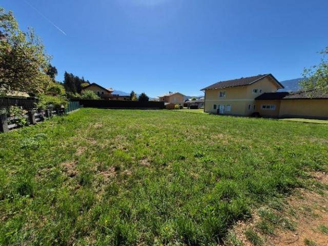 Großes, sonniges Grundstück mit Rasenfläche und einem Haus im Hintergrund unter blauem Himmel.