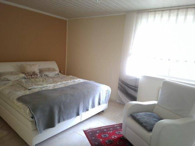 Gemütliches Schlafzimmer mit Doppelbett, Sessel und großem Fenster für viel Tageslicht.