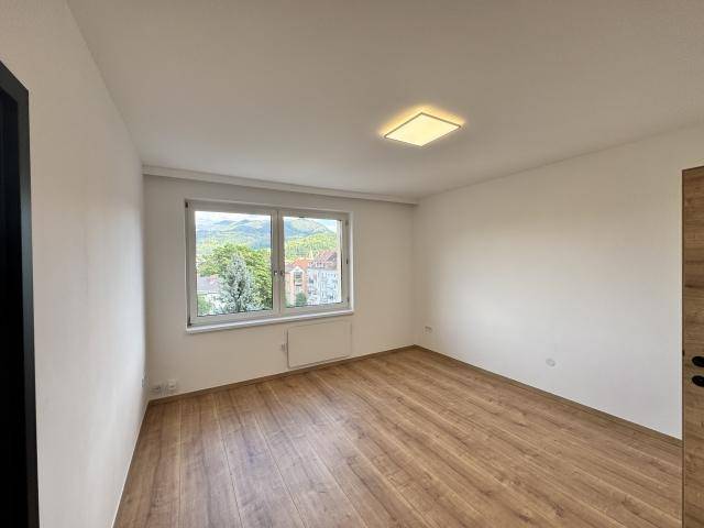Helles und leeres Zimmer mit Laminatboden, weißen Wänden und einem Fenster mit Bergblick.