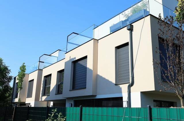 Reihe moderner Stadthäuser mit Flachdach, großen Fenstern und Glasgeländern auf den Dachterrassen.
