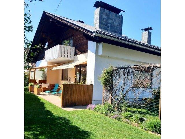 Hausfassade mit Balkon, Terrasse und gepflegtem Rasen im Vorgarten.