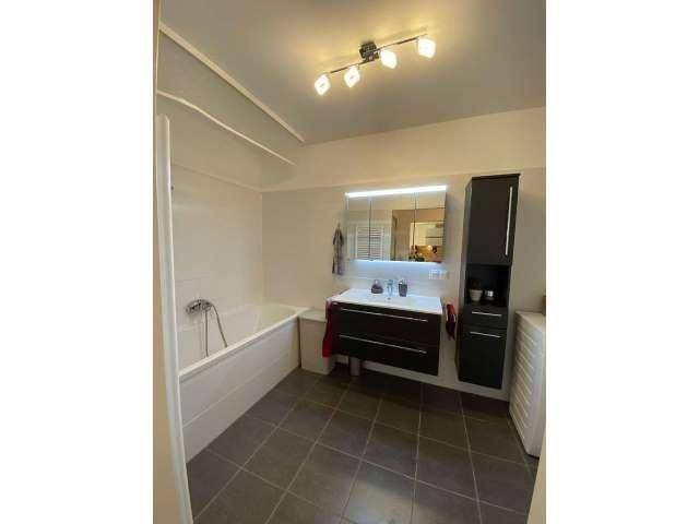 Funktionales Badezimmer mit Badewanne, modernem Waschtisch und dunklen Bodenfliesen.