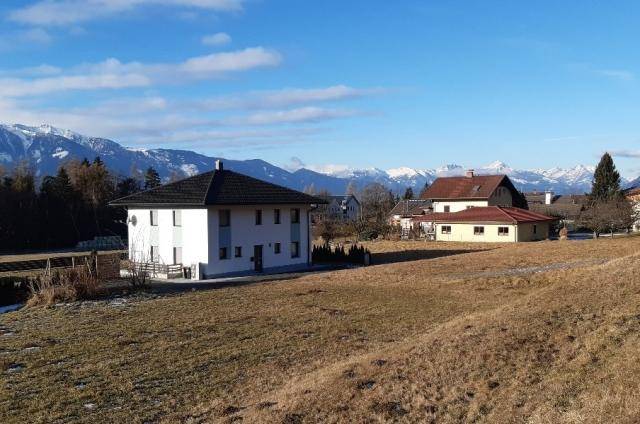 Modernes weißes Haus mit dunklem Dach und weitem Blick auf schneebedeckte Berge und umliegende Häuser.