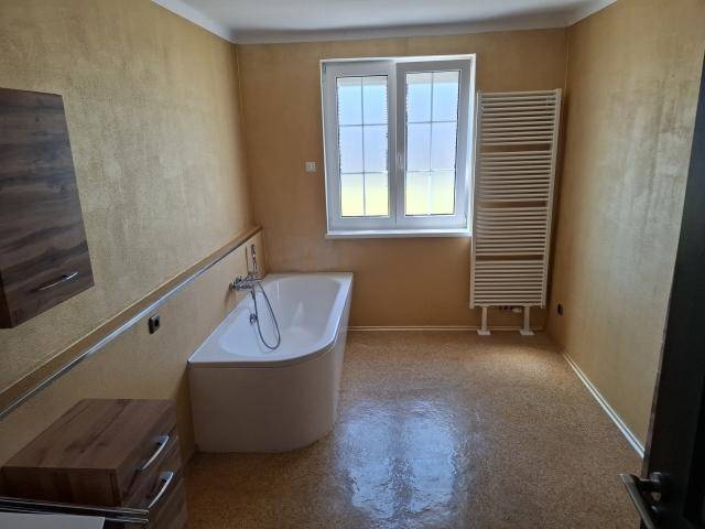 Badezimmer mit Badewanne, Fenster und beheiztem Handtuchhalter in warmen Farbtönen.