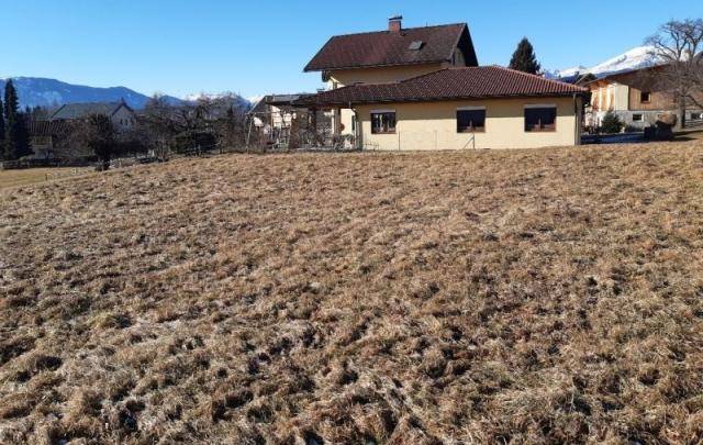 Haus mit rotem Dach und Terrasse, umgeben von einem trockenen Feld mit Bergblick im Hintergrund.