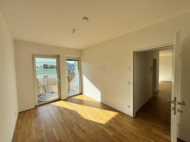 Heller Raum mit Parkettboden und großen Glastüren, die Zugang zu einem Außenbereich bieten.