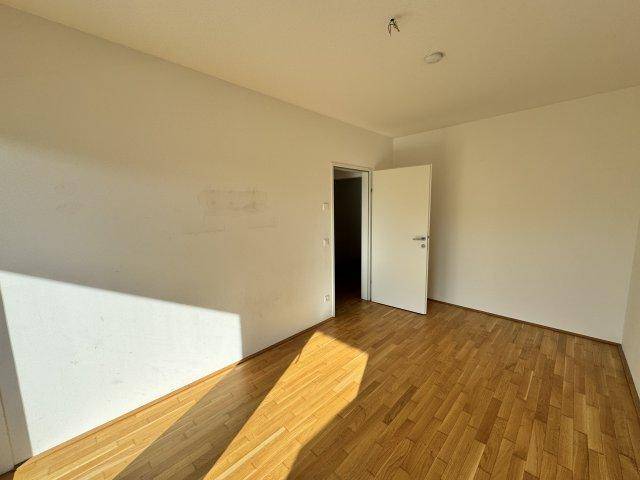 Sonniger Raum mit Holzboden und weißen Wänden, ideal als Schlafzimmer oder Arbeitszimmer.