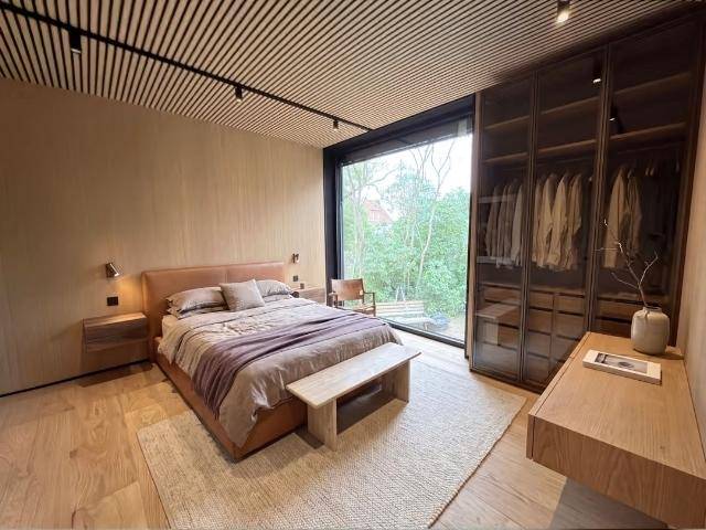 Elegantes Schlafzimmer mit Holzboden, Glas-Einbauschränken und raumhohen Fenstern mit Blick auf die Bäume.