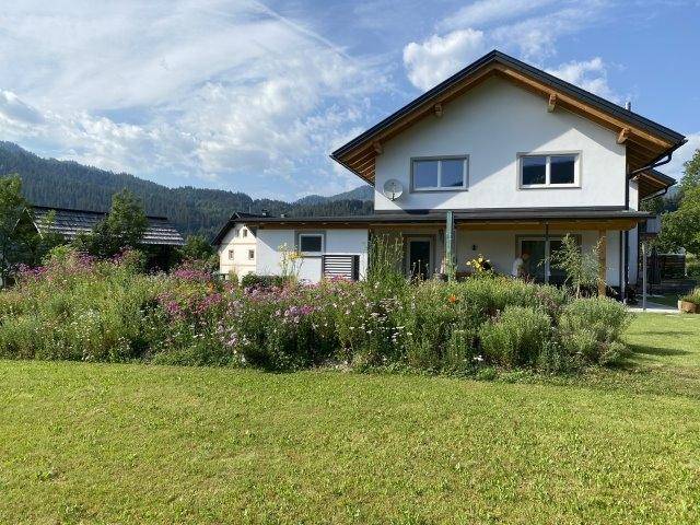 Weitläufiger Garten mit Rasenfläche, blühenden Beeten und einem modernen Einfamilienhaus im Hintergrund.
