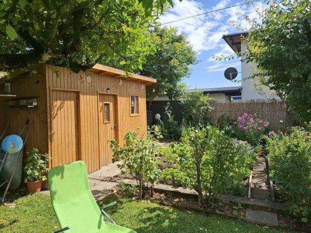 Gepflegter Garten mit Holzschuppen, Rasenfläche und üppiger Bepflanzung.