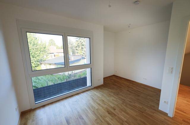 Helles Schlafzimmer mit großem Fenster und Blick ins Grüne, ausgestattet mit Parkettboden.