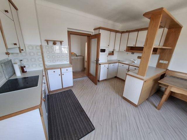 Funktionale Küche mit weißen Schränken, Holzakzenten und hellem Laminatboden.